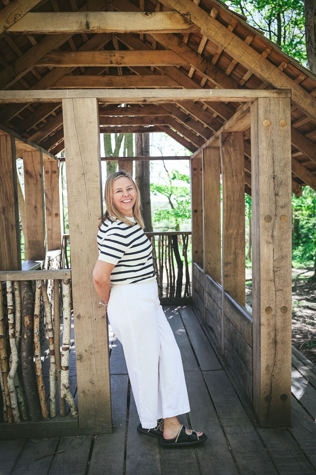 Sharon Forrester smiling inside a wooden structure, wearing a striped top